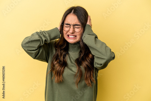 Young caucasian woman isolated on yellow background covering ears with hands. © Asier