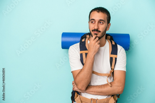 Young caucasian hiker man isolated on blue background relaxed thinking about something looking at a copy space.