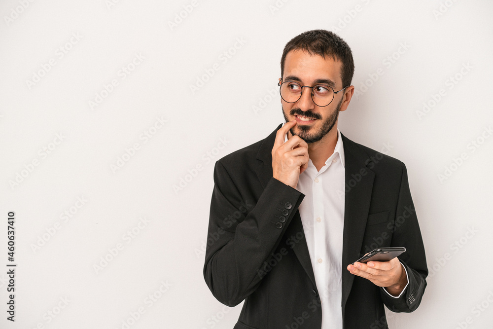 Young business man holding a mobile phone isolated on white background relaxed thinking about something looking at a copy space. Young business man holding a mobile phone isolated on white background relaxed thinking about something looking at a copy space.