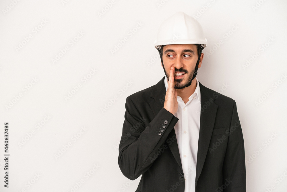 Young architect man wearing a construction helmet isolated on white background is saying a secret hot braking news and looking aside Young architect man wearing a construction helmet isolated on white background is saying a secret hot braking news and looking aside