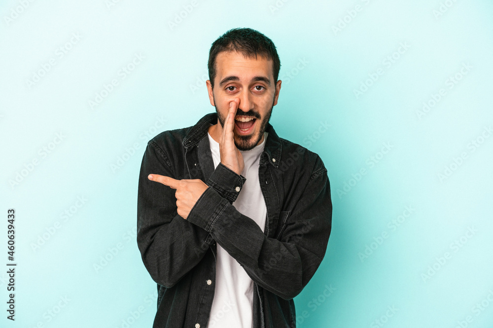 Young caucasian man isolated on blue background saying a gossip, pointing to side reporting something. Young caucasian man isolated on blue background saying a gossip, pointing to side reporting something.