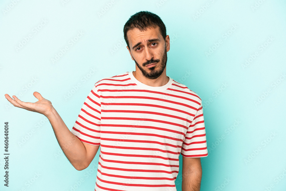 Young caucasian man isolated on blue background doubting and shrugging shoulders in questioning gesture. Young caucasian man isolated on blue background doubting and shrugging shoulders in questioning gesture.