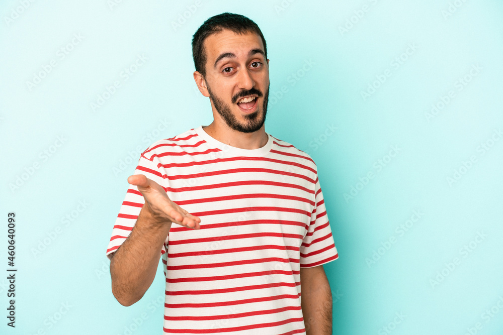 Young caucasian man isolated on blue background stretching hand at camera in greeting gesture. Young caucasian man isolated on blue background stretching hand at camera in greeting gesture.