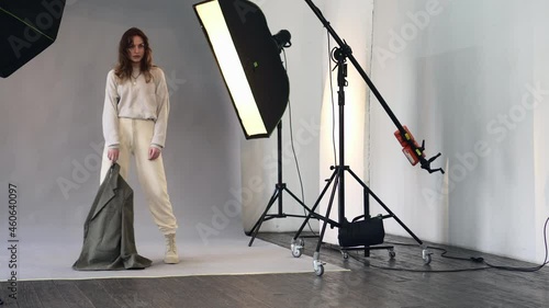 Young pretty woman model poses for a photographer at a photo studio during a photo shoot. Flashes of studio lights.
