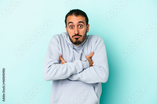 Young caucasian man isolated on blue background shrugs shoulders and open eyes confused.