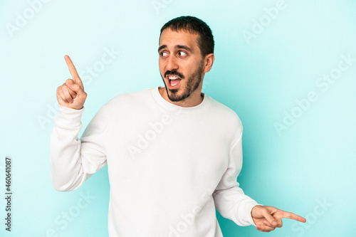 Young caucasian man isolated on blue background pointing to different copy spaces, choosing one of them, showing with finger.