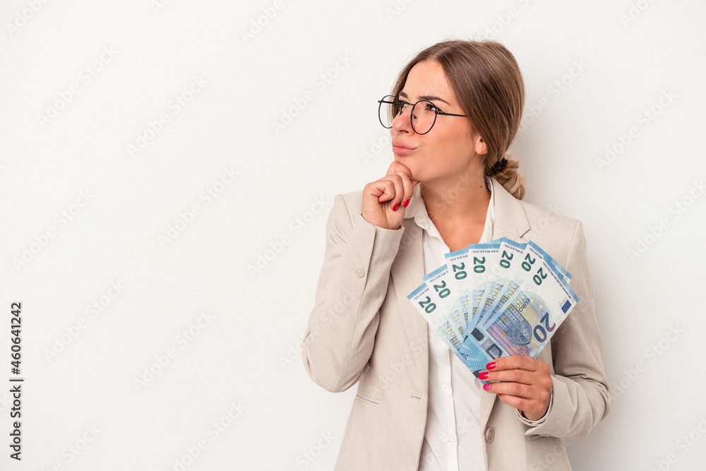 Young Russian business woman holding banknotes isolated on white background looking sideways with doubtful and skeptical expression. Young Russian business woman holding banknotes isolated on white background looking sideways with doubtful and skeptical expression.