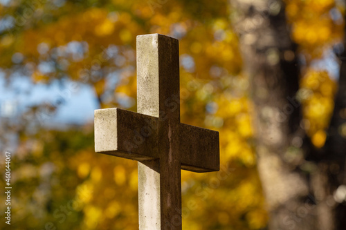 Stone cross in an old abandoned cemetery on a sunny autumn day with golden foliage