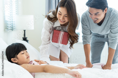 Asian Happy family, young parents surprise sleep daughter with gift. 