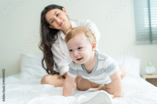 Caucasian mother play with cute baby boy child on infant bed at home. 