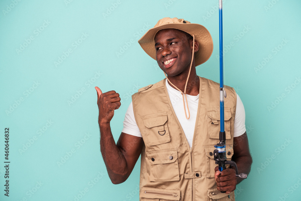 Young African American fisherman holding rod isolated on blue background points with thumb finger away, laughing and carefree. Young African American fisherman holding rod isolated on blue background points with thumb finger away, laughing and carefree.