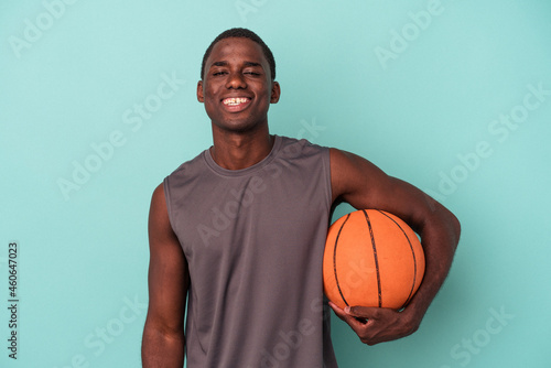 Young African American man playing basketball isolated on blue background happy, smiling and cheerful.