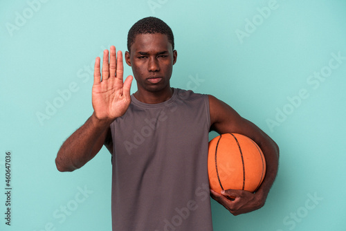 Young African American man playing basketball isolated on blue background standing with outstretched hand showing stop sign, preventing you. © Asier