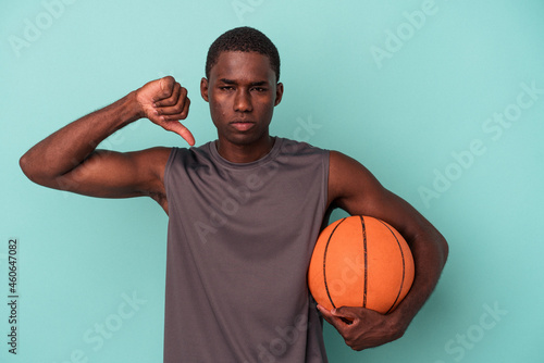 Young African American man playing basketball isolated on blue background showing a dislike gesture, thumbs down. Disagreement concept.