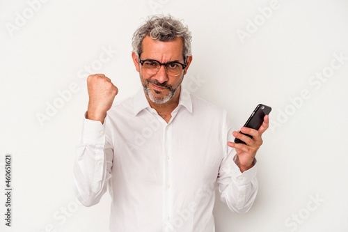 Middle age caucasian business man holding a mobile phone isolated on white background  showing fist to camera, aggressive facial expression. © Asier
