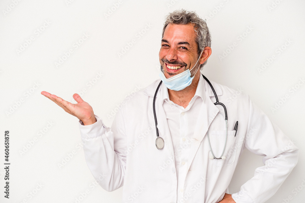 Middle age doctor man wearing a mask for virus isolated on white background showing a copy space on a palm and holding another hand on waist. Middle age doctor man wearing a mask for virus isolated on white background showing a copy space on a palm and holding another hand on waist.