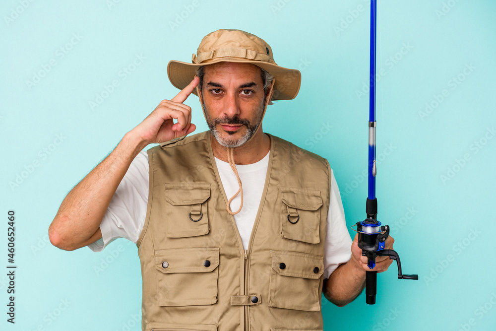 Middle age caucasian fisherman holding rod isolated on blue background  pointing temple with finger, thinking, focused on a task.