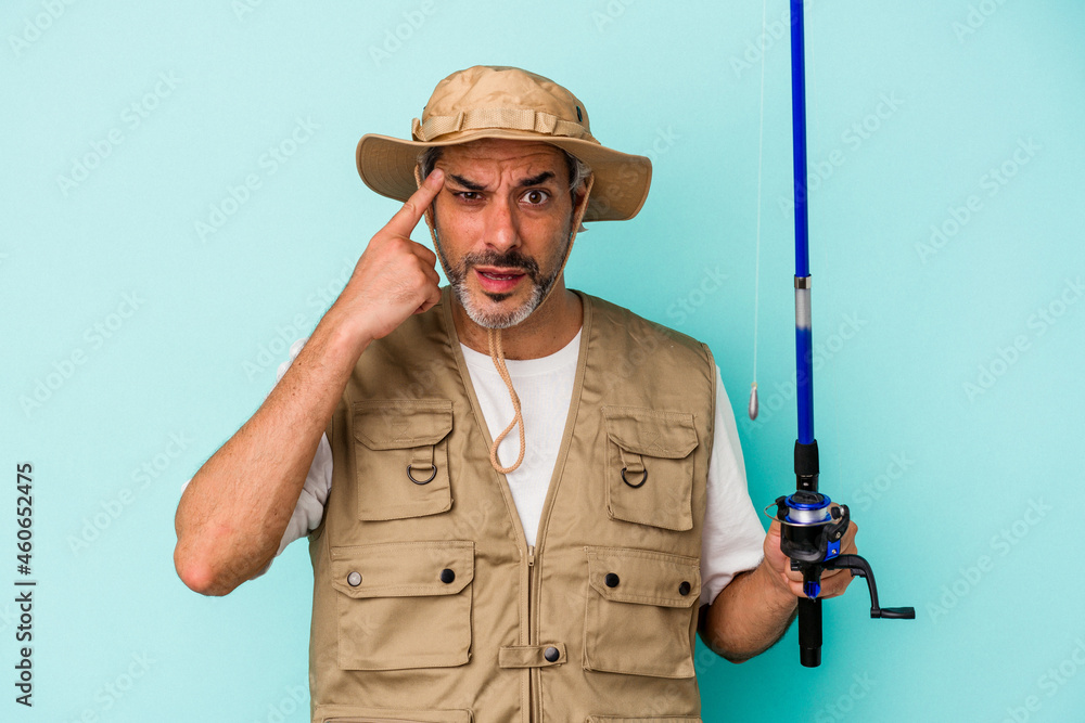 Middle age caucasian fisherman holding rod isolated on blue background  showing a disappointment gesture with forefinger.