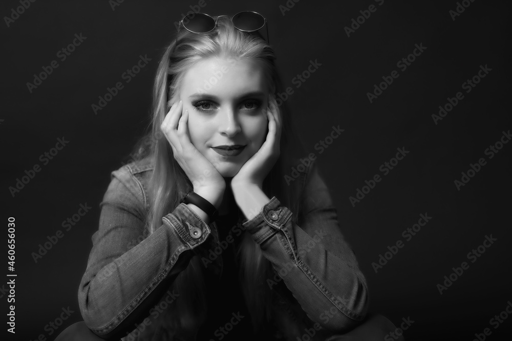 Black and white portrait of smiling attractive young woman with sunglasses on her head is sitting on the black background. Horizontally. Black and white portrait of smiling attractive young woman with sunglasses on her head is sitting on the black background. Horizontally.