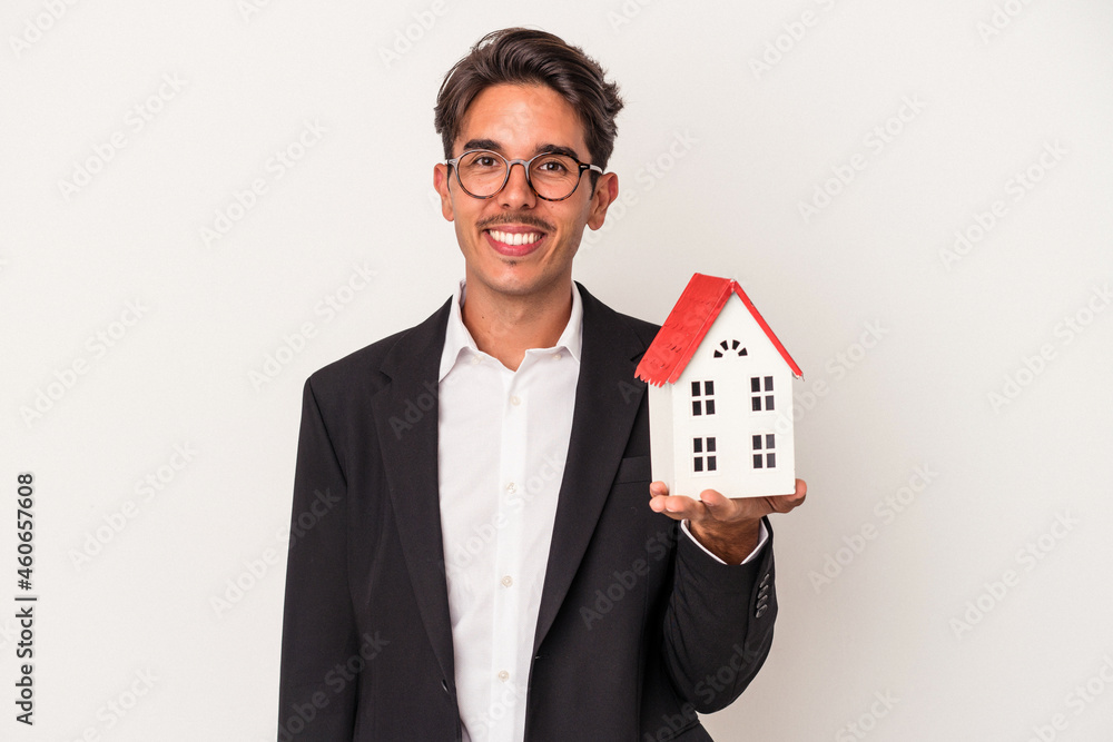 Young mixed race business man holding a toy house isolated on white background happy, smiling and cheerful. Young mixed race business man holding a toy house isolated on white background happy, smiling and cheerful.