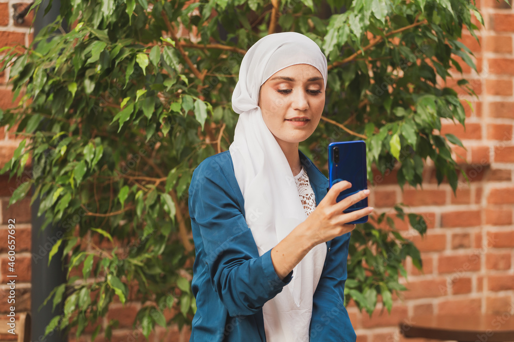 Muslim young woman wearing hijab head scarf in city texting cell phone Muslim young woman wearing hijab head scarf in city texting cell phone