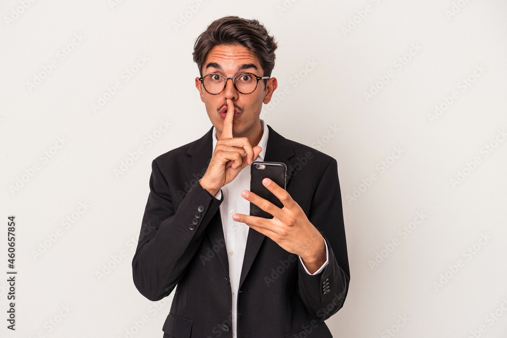 Young mixed race business man holding mobile phone isolated on white background keeping a secret or asking for silence. Young mixed race business man holding mobile phone isolated on white background keeping a secret or asking for silence.
