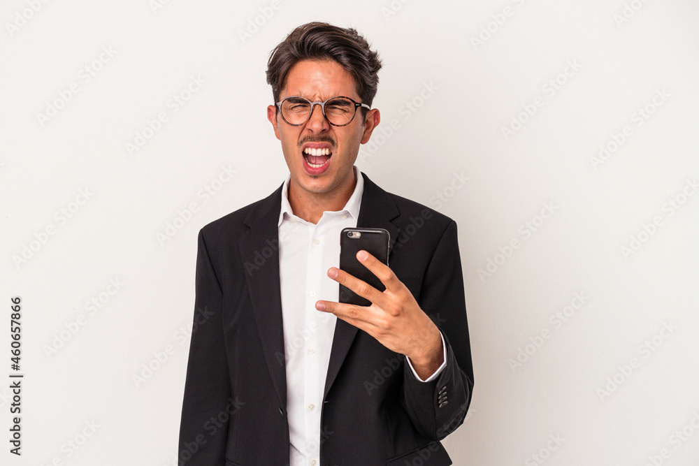 Young mixed race business man holding mobile phone isolated on white background screaming very angry and aggressive. Young mixed race business man holding mobile phone isolated on white background screaming very angry and aggressive.