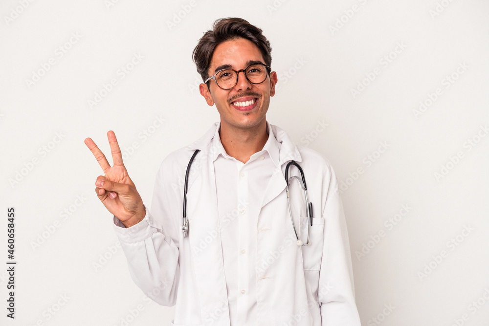 Young mixed race doctor man isolated on white background joyful and carefree showing a peace symbol with fingers. Young mixed race doctor man isolated on white background joyful and carefree showing a peace symbol with fingers.