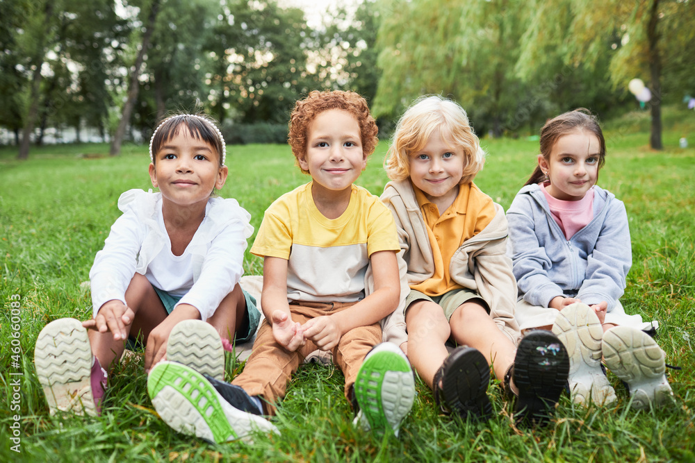 Full length portrait of diverse group of kids sitting on grass in park and looking at camera Full length portrait of diverse group of kids sitting on grass in park and looking at camera
