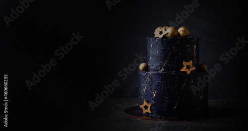 Black bunk cake on the dark black background with golden stars and spheres decoration on top. luxurious birthday cake