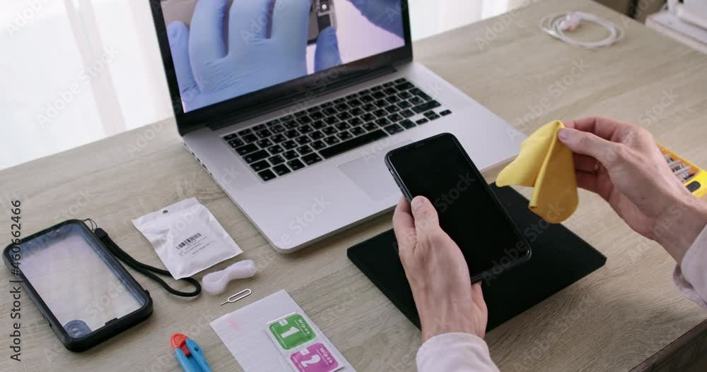 Men's hands wipe the phone screen against the background of a training phone repair video. High quality 4k footage Men's hands wipe the phone screen against the background of a training phone repair video. High quality 4k footage