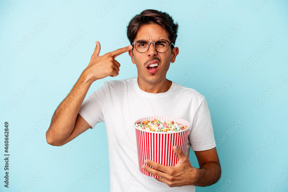 Young mixed race man eating popcorns isolated on blue background showing a disappointment gesture with forefinger. Young mixed race man eating popcorns isolated on blue background showing a disappointment gesture with forefinger.