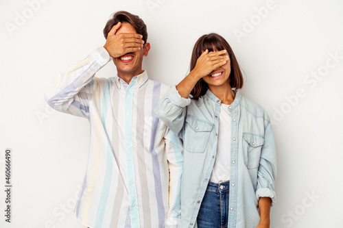 Young mixed race couple isolated on white background covers eyes with hands, smiles broadly waiting for a surprise.