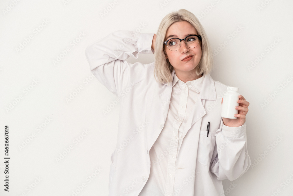 Young pharmacist woman holding pills isolated on white background touching back of head, thinking and making a choice. Young pharmacist woman holding pills isolated on white background touching back of head, thinking and making a choice.