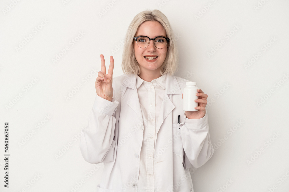 Young pharmacist woman holding pills isolated on white background showing number two with fingers. Young pharmacist woman holding pills isolated on white background showing number two with fingers.