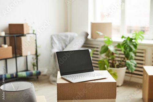 Background image of opened laptop with blank screen on cardboard boxes in new home, moving and relocation concept, copy space