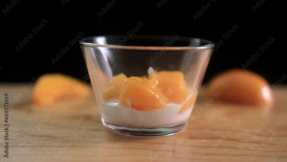 Peach slices falling into glass cup with yogurt above wooden surface Peach slices falling into glass cup with yogurt above wooden surface