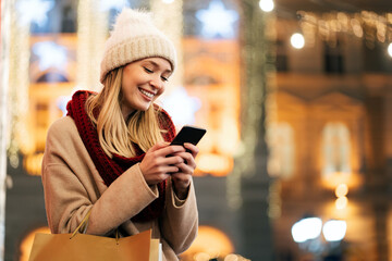 Portrait of young smiling beautiful woman using smartphone on the street at winter