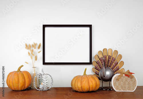Mock up black frame hanging from a white wall with thanksgiving turkey, pumpkin and autumn decor on a wood shelf. Fall concept. Copy space.