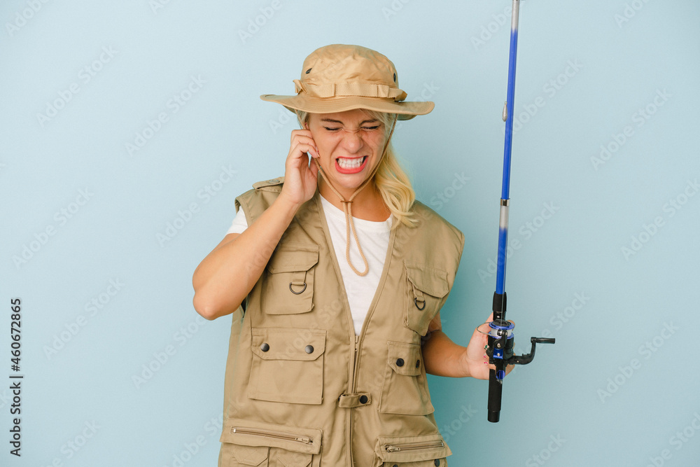 Young Russian fisherwoman isolated on blue background covering ears with hands. Young Russian fisherwoman isolated on blue background covering ears with hands.