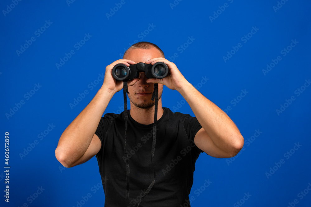 Young man over isolated blue wall and looking in the distance with binoculars. Young man over isolated blue wall and looking in the distance with binoculars.