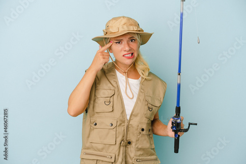 Young Russian fisherwoman isolated on blue background showing a disappointment gesture with forefinger.