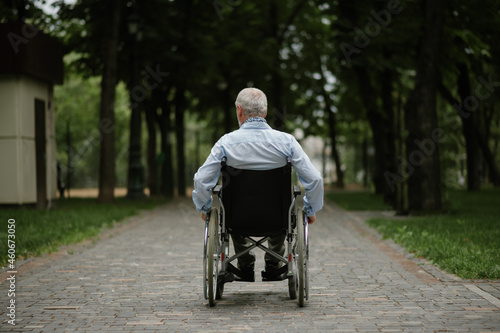 Adult disabled man in wheelchair walking in park