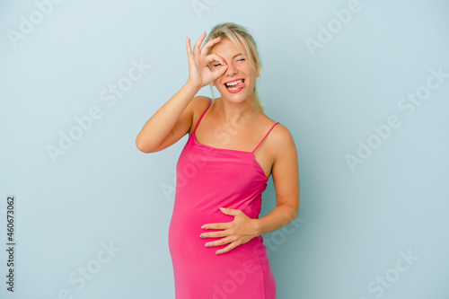 Young Russian woman pregnant isolated on blue background excited keeping ok gesture on eye.
