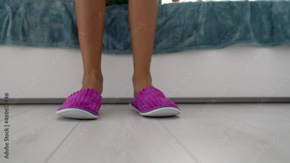 Female feet wearing pink bedroom slippers at bed on floor, houseshoes Female feet wearing pink bedroom slippers at bed on floor, houseshoes