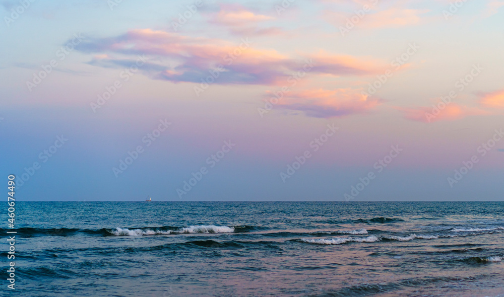 Obraz premium minimalist see and sky with sunset colors some clouds with sailboat sailing in the horizon