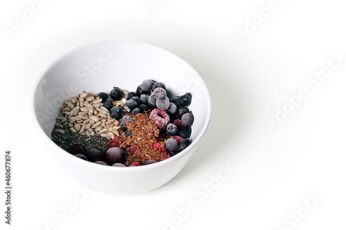 Healthy breakfast in a plate. Chia seeds, flax, sunflower seeds, nuts, frozen berries: irga, cherry and raspberry in a white plate on a white isolated background. Vegan foo