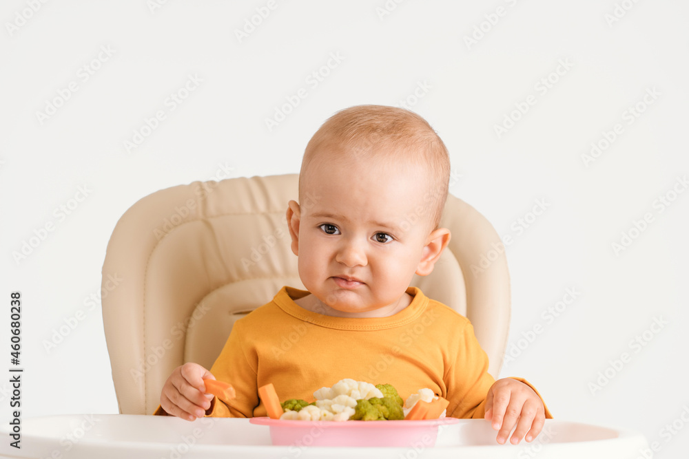 Portrait of a disgruntled baby at the dinner table. A child aged 12-17 months does not want to eat boiled vegetables
