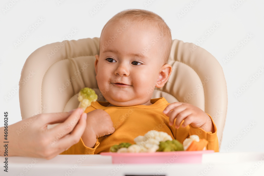 Mom's hand gives a baby sitting on a feeding chair boiled broccoli Mom's hand gives a baby sitting on a feeding chair boiled broccoli