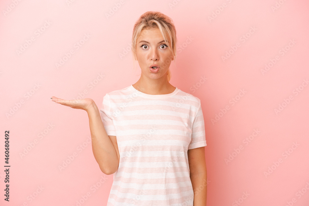 Young Russian woman isolated on pink background impressed holding copy space on palm. Young Russian woman isolated on pink background impressed holding copy space on palm.